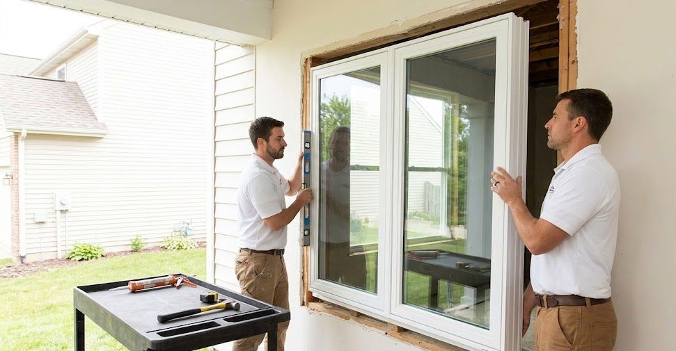 Active photograph of two contractors carefully installing a modern vinyl window unit into a house framing.